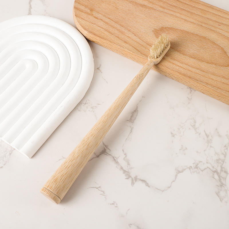 Round bamboo toothbrush with light boar bristles on a wooden board and marble surface