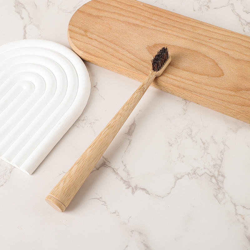 Round bamboo toothbrush with dark horsehair bristles on a wooden board and marble surface